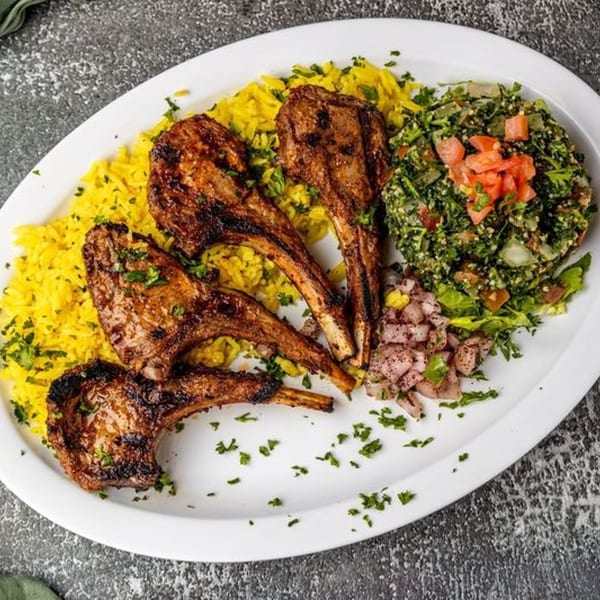 Grilled lamb chops with yellow rice, tabbouleh salad, and diced onions on a white platter.