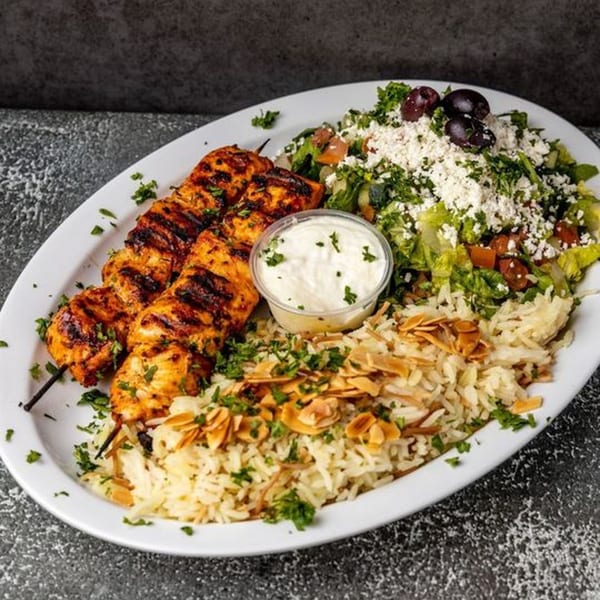 Two chicken skewers, rice with almonds, a side salad with feta and olives, and a dip.