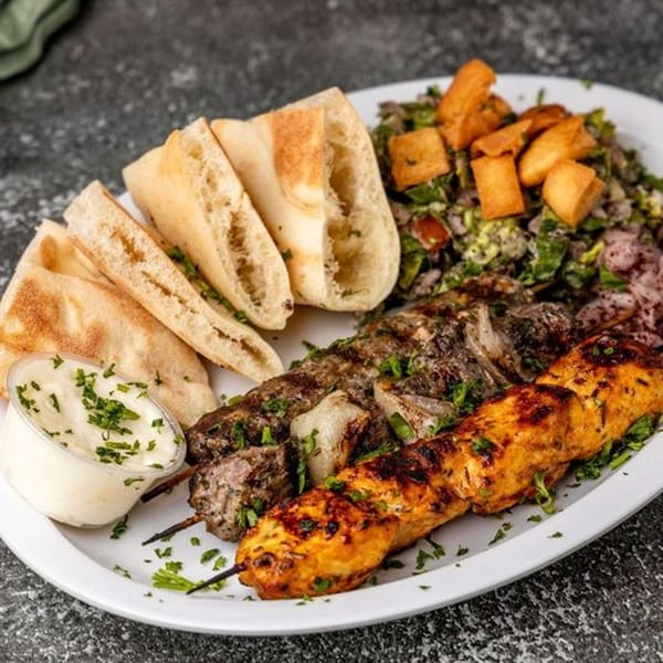 Pita Shop's Mediterranean platter with two skewers of grilled meat, pita bread, salad, and sauce.