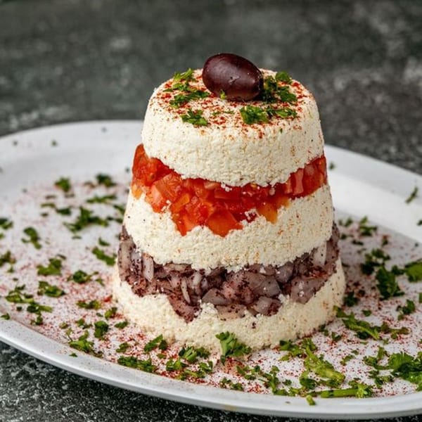 Layered Mediterranean dip with white cheese, diced tomatoes, red onions, and an olive on top.