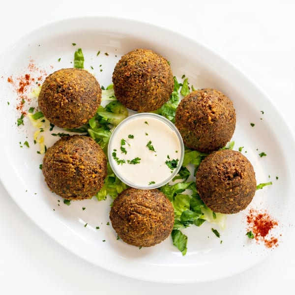 Six falafel balls on a bed of lettuce with a side of white dipping sauce.