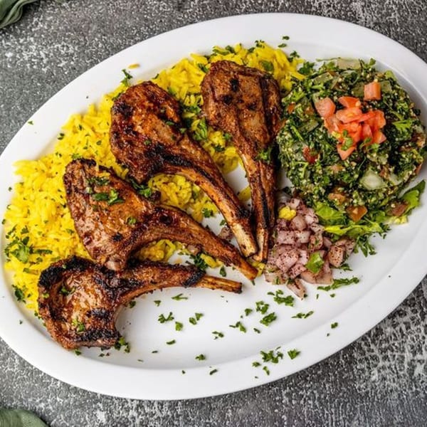 Grilled lamb chops with yellow rice, tabbouleh salad, and diced onions on a white platter.