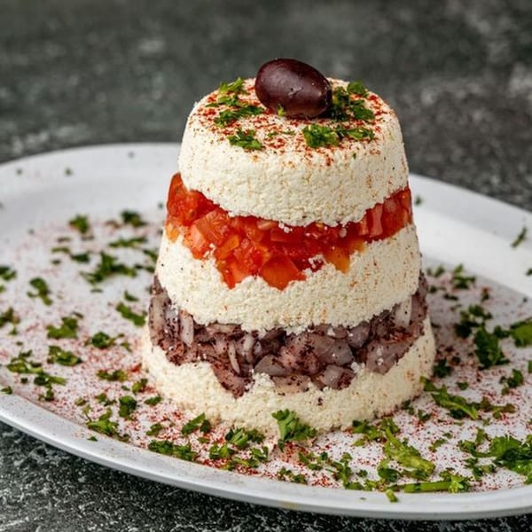 Layered Mediterranean dip with white cheese, diced tomatoes, and dark olive tapenade, garnished with an olive.