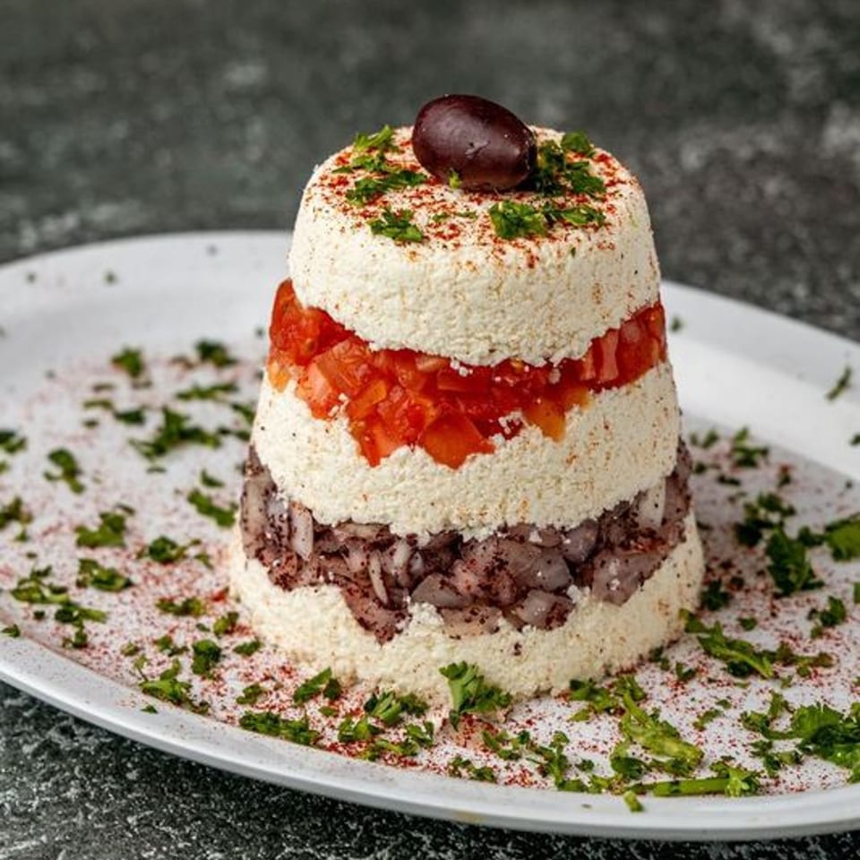 Layered Mediterranean dip with white cheese, diced tomatoes, and dark olive tapenade, garnished with an olive.