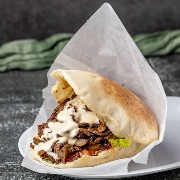 Pita Shop's Mediterranean shawarma in pita bread with meat, lettuce, tomatoes, and white sauce.