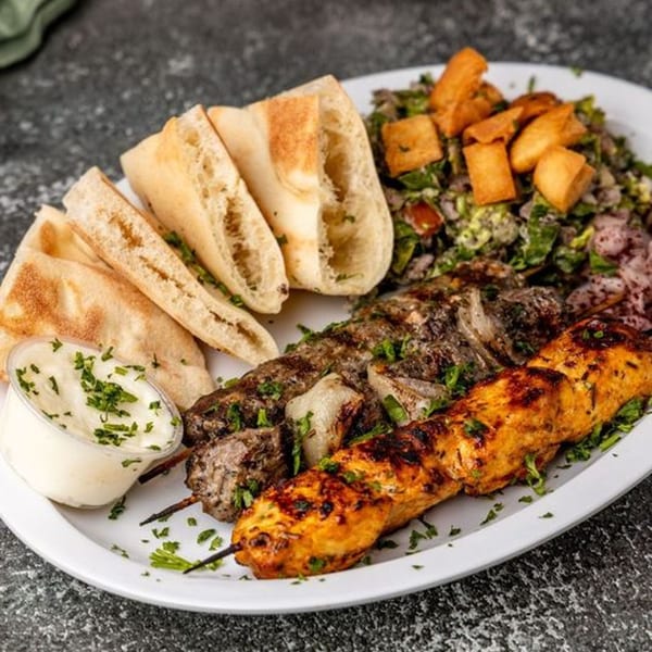 Mediterranean platter with chicken and beef kebabs, pita bread, salad, and a side of sauce.
