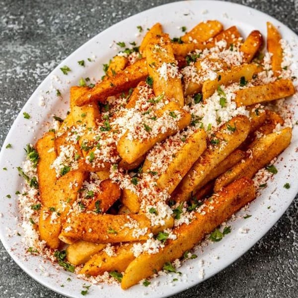 A white platter of golden-brown Mediterranean fries topped with crumbled feta, paprika, and parsley.