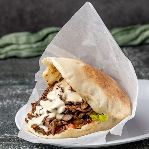 Pita Shop's Mediterranean pita sandwich, filled with meat, lettuce, tomatoes, and white sauce.
