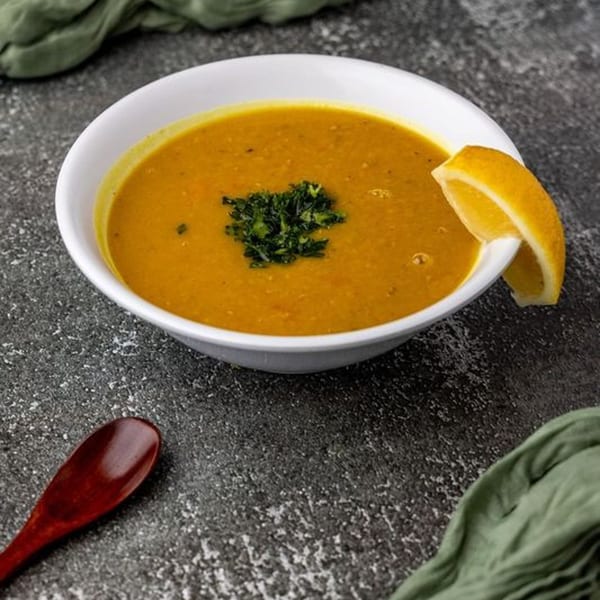 A bowl of golden lentil soup garnished with parsley and a lemon wedge, with a wooden spoon.
