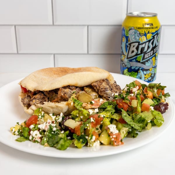 A pita sandwich with meat and vegetables, a side salad, and a can of Brisk Iced Tea.